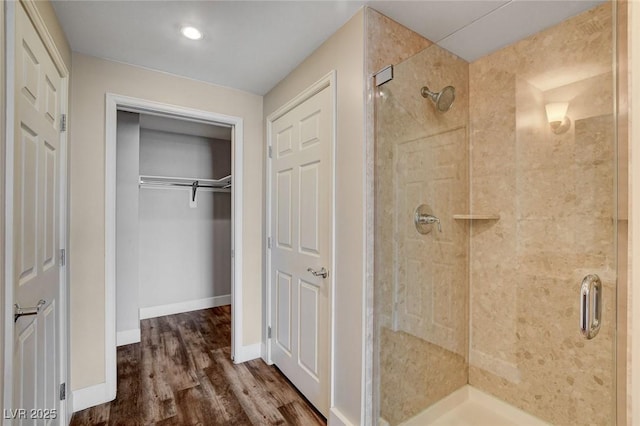 bathroom featuring a shower stall, wood finished floors, baseboards, a spacious closet, and recessed lighting