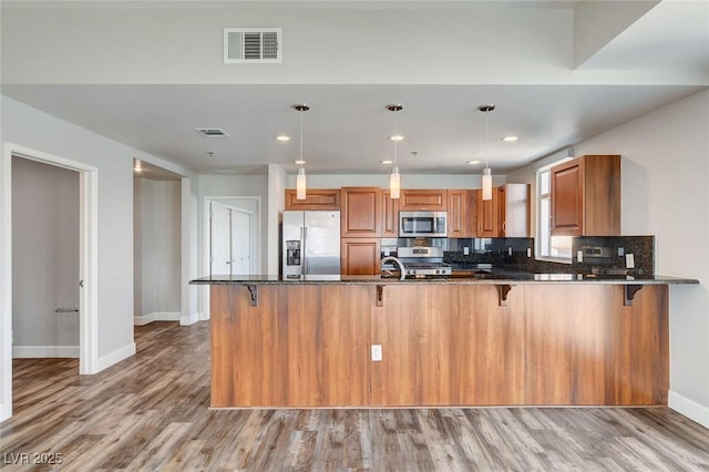 kitchen with stainless steel appliances, brown cabinets, baseboards, dark stone countertops, and recessed lighting