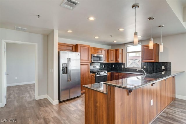 kitchen with appliances with stainless steel finishes, a peninsula, brown cabinetry, baseboards, and light wood-type flooring