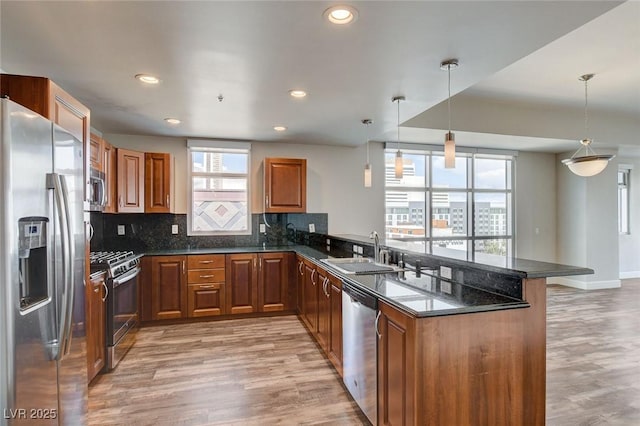 kitchen with stainless steel appliances, a sink, a peninsula, light wood finished floors, and brown cabinets