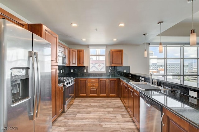 kitchen with appliances with stainless steel finishes, a sink, light wood-type flooring, brown cabinets, and recessed lighting