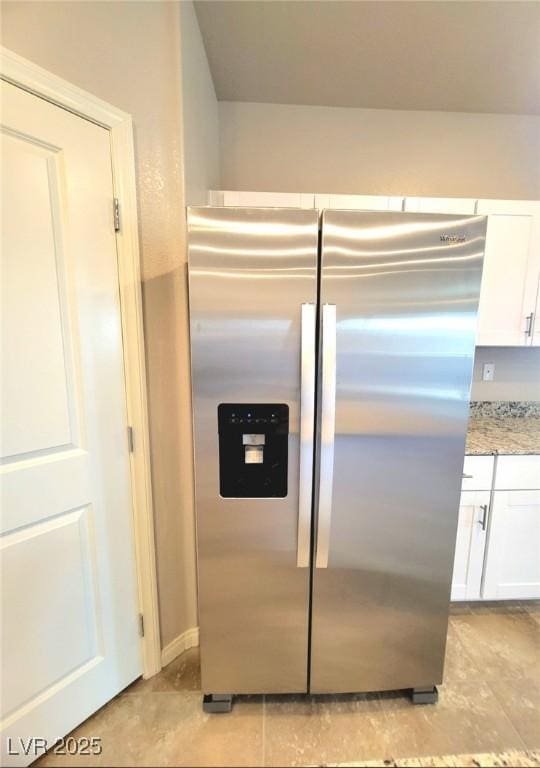 kitchen featuring stainless steel fridge, white cabinetry, light stone counters, and light tile patterned floors