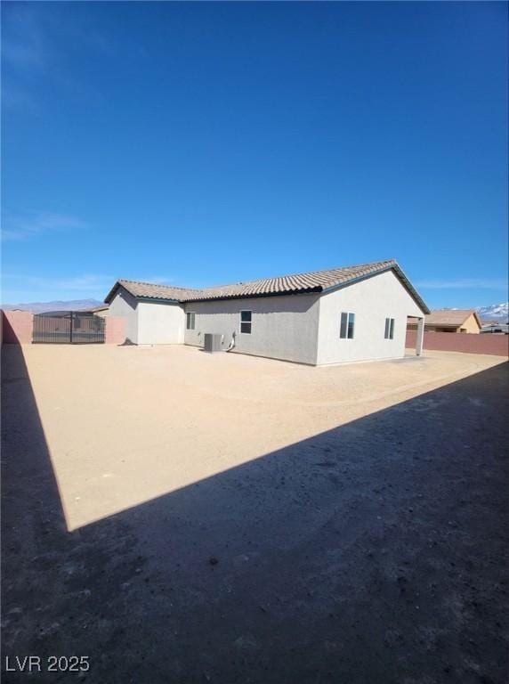 back of house with stucco siding, a tile roof, and fence