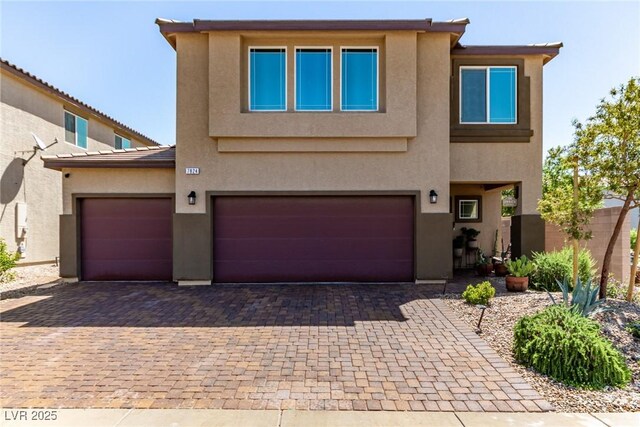 view of front of house with decorative driveway, stucco siding, an attached garage, and fence