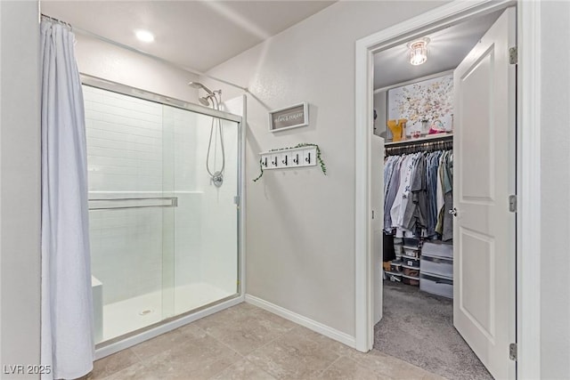 full bathroom with a stall shower, a walk in closet, baseboards, and tile patterned floors
