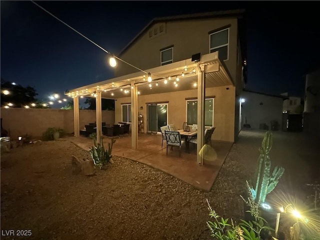 back of house at night featuring stucco siding, a patio, and fence