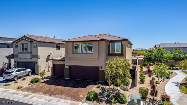 traditional-style home with an attached garage, stucco siding, a tile roof, and decorative driveway