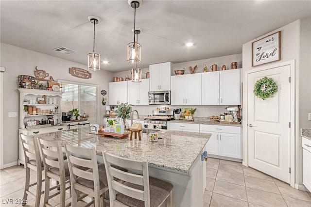 kitchen with stainless steel appliances, light tile patterned flooring, a kitchen bar, and white cabinetry