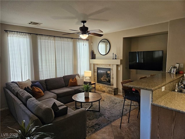 tiled living room featuring a ceiling fan, a tiled fireplace, and baseboards