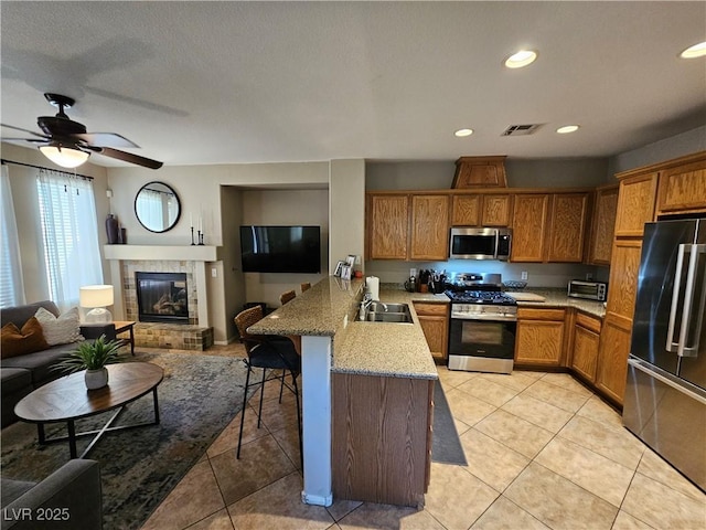 kitchen featuring appliances with stainless steel finishes, a peninsula, open floor plan, brown cabinets, and a breakfast bar area