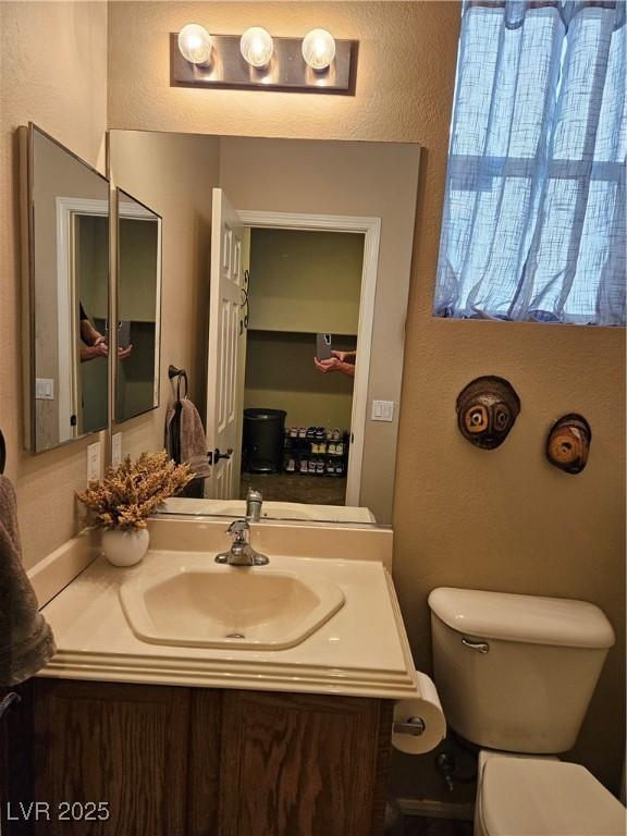 bathroom featuring toilet, a textured wall, and vanity