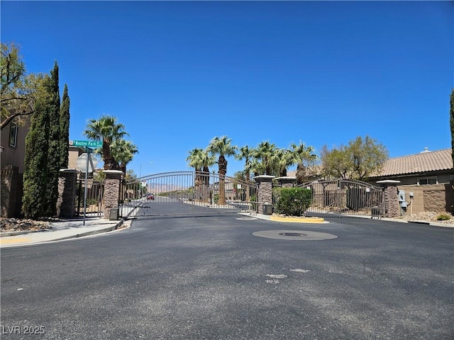 view of asphalt street featuring a gate, curbs, a gated entry, and sidewalks