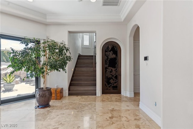 entrance foyer featuring crown molding, arched walkways, stairway, and baseboards