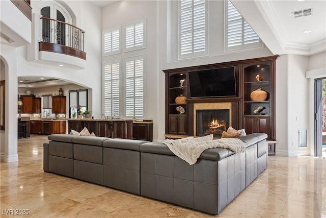 living area with light marble finish flooring, a towering ceiling, arched walkways, a high end fireplace, and crown molding