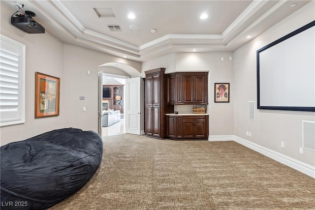 home theater room featuring a tray ceiling, ornamental molding, light carpet, recessed lighting, and arched walkways