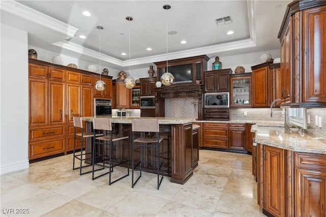 kitchen with stainless steel appliances, a kitchen breakfast bar, a center island with sink, decorative backsplash, and a raised ceiling