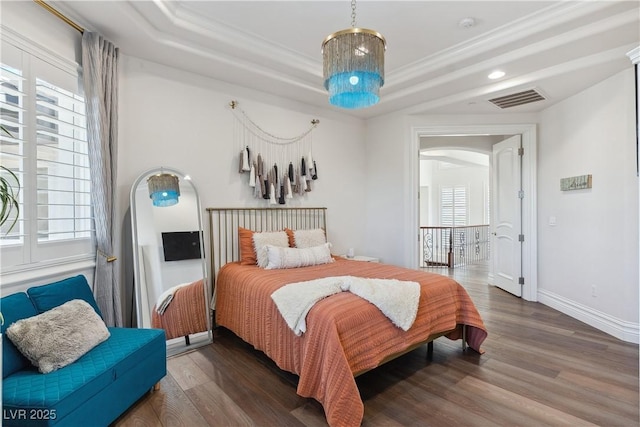 bedroom with arched walkways, wood finished floors, a tray ceiling, baseboards, and crown molding