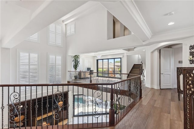 hallway featuring wood finished floors, baseboards, an upstairs landing, arched walkways, and a towering ceiling