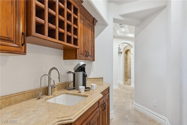kitchen with a sink, brown cabinets, arched walkways, light tile patterned flooring, and recessed lighting