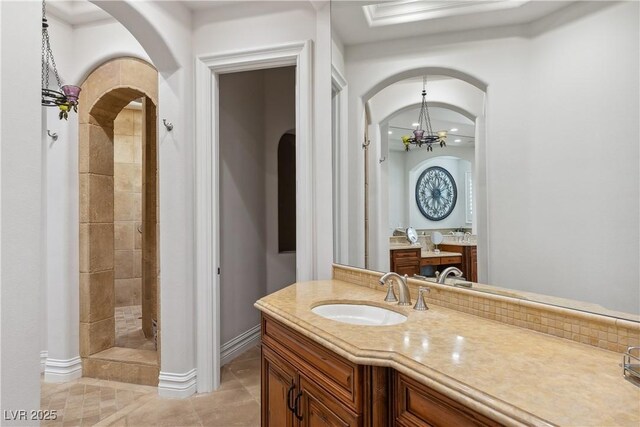 bathroom with tile patterned flooring, tiled shower, vanity, baseboards, and a chandelier