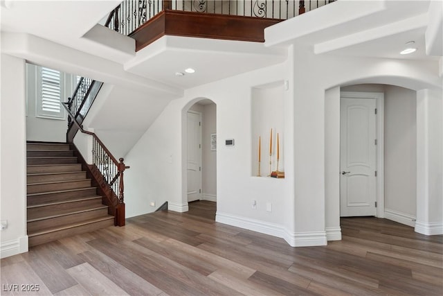unfurnished living room with arched walkways, wood finished floors, stairway, and baseboards