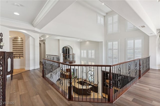 hall with baseboards, wood finished floors, crown molding, and arched walkways