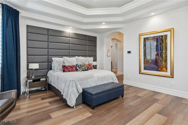bedroom with arched walkways, crown molding, wood finished floors, a tray ceiling, and recessed lighting