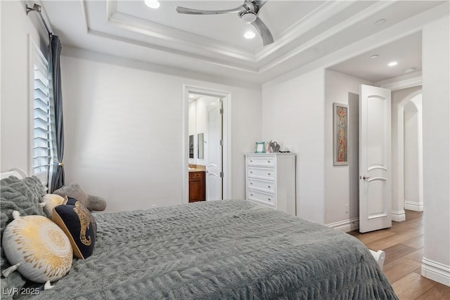 bedroom with light wood-type flooring, crown molding, recessed lighting, a raised ceiling, and connected bathroom