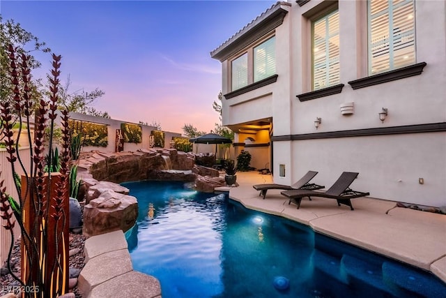 pool at dusk featuring a patio and fence