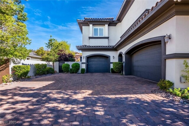exterior space with stucco siding, decorative driveway, fence, an attached garage, and a tiled roof