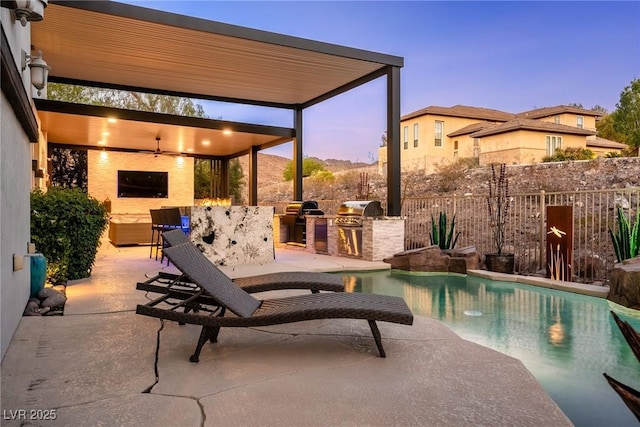 pool at dusk featuring exterior kitchen, fence, a patio area, ceiling fan, and a grill