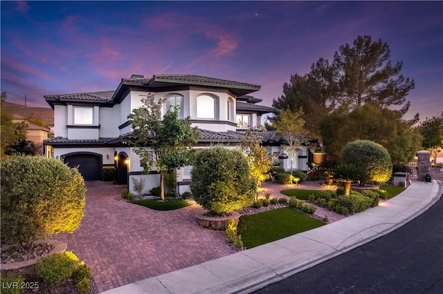mediterranean / spanish home with a tile roof, stucco siding, a garage, and decorative driveway