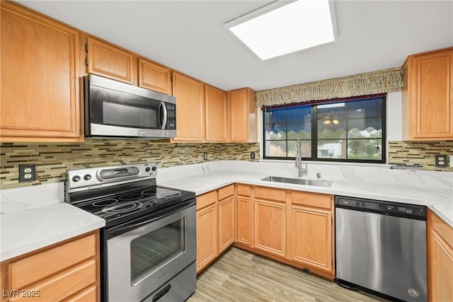 kitchen with stainless steel appliances, a sink, light wood-style flooring, and decorative backsplash