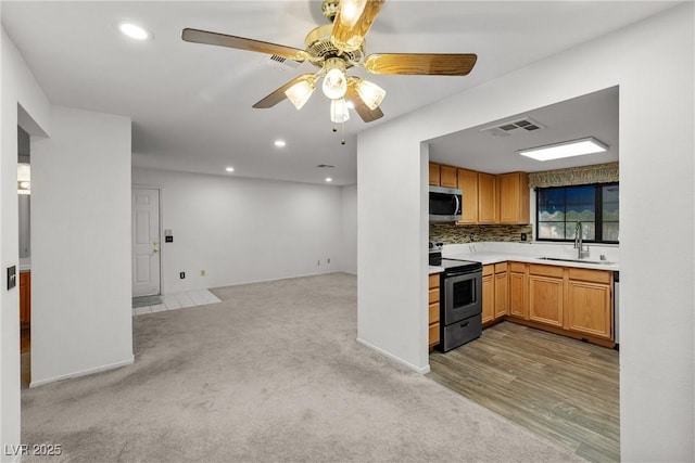 kitchen with stainless steel appliances, a sink, open floor plan, light countertops, and recessed lighting