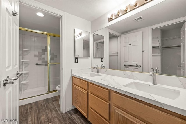 full bath featuring a stall shower, toilet, wood finished floors, double vanity, and baseboards