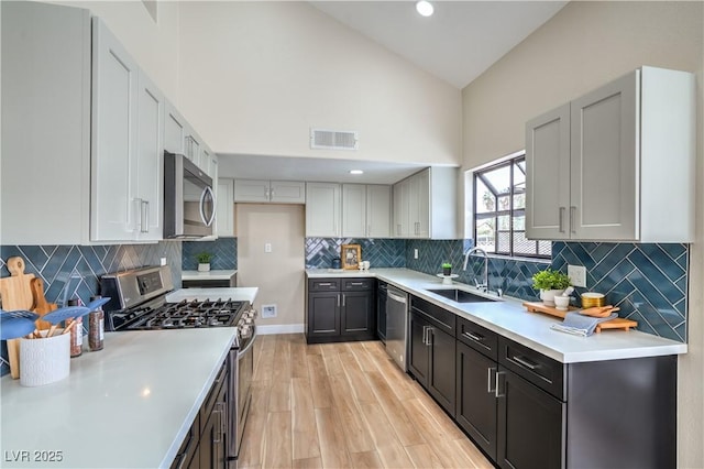 kitchen with appliances with stainless steel finishes, a sink, light countertops, light wood-type flooring, and high vaulted ceiling