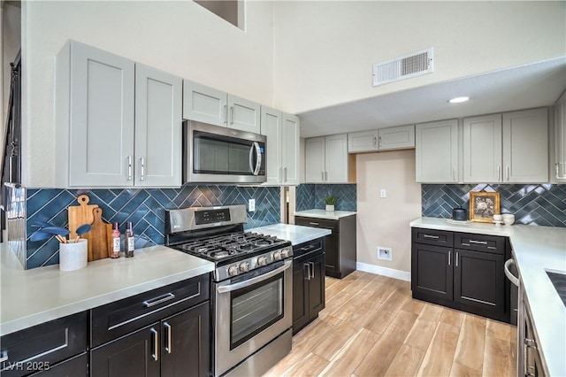 kitchen featuring stainless steel appliances, light countertops, light wood-type flooring, backsplash, and a high ceiling