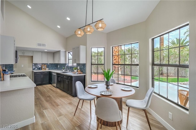 kitchen featuring dishwasher, backsplash, light countertops, light wood-style floors, and high vaulted ceiling