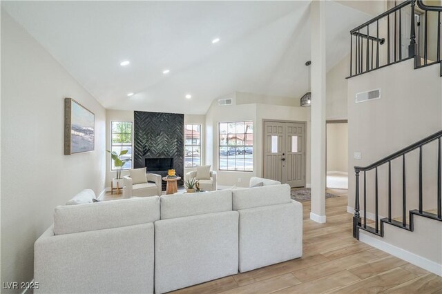 living room featuring a large fireplace, stairway, light wood-style flooring, high vaulted ceiling, and baseboards