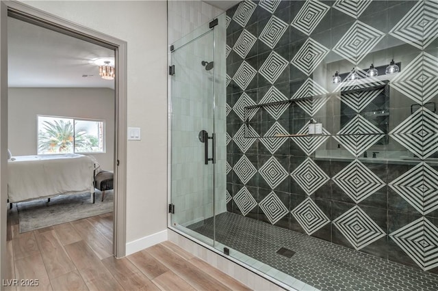 bathroom featuring connected bathroom, wood finished floors, a stall shower, and baseboards