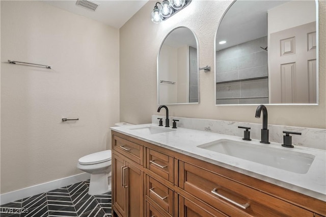 bathroom featuring toilet, double vanity, baseboards, and a tile shower