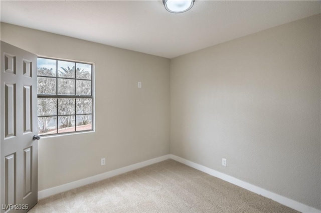 spare room featuring light colored carpet and baseboards