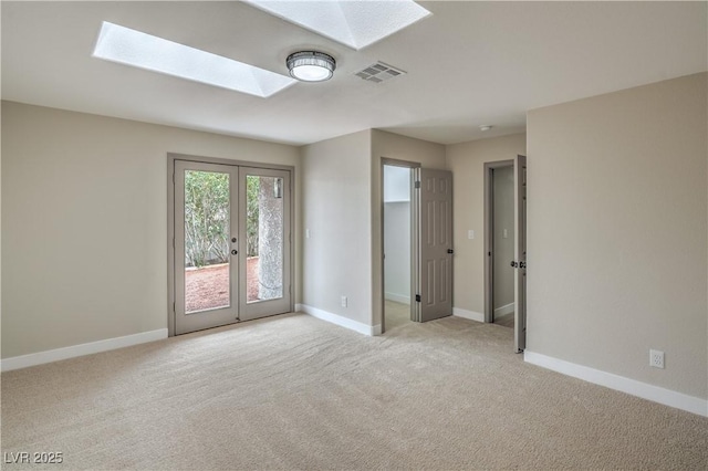 empty room featuring a skylight, light carpet, baseboards, and french doors