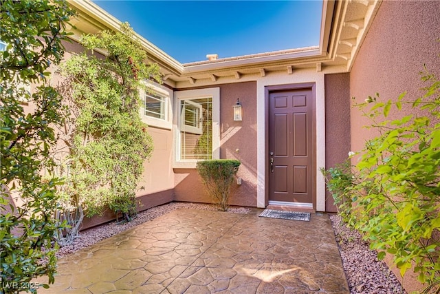 view of exterior entry featuring stucco siding and a patio