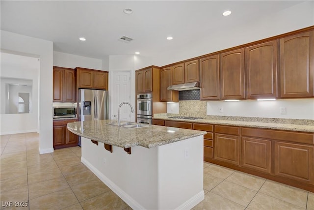 kitchen featuring appliances with stainless steel finishes, a sink, under cabinet range hood, light tile patterned floors, and light stone counters