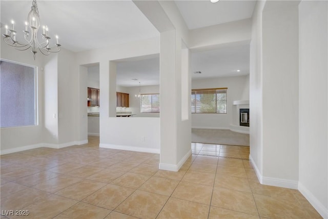 unfurnished living room featuring a chandelier, light tile patterned floors, a glass covered fireplace, and baseboards