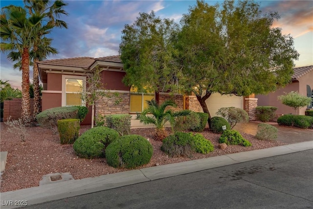 view of front of house with stucco siding, stone siding, a tiled roof, concrete driveway, and fence
