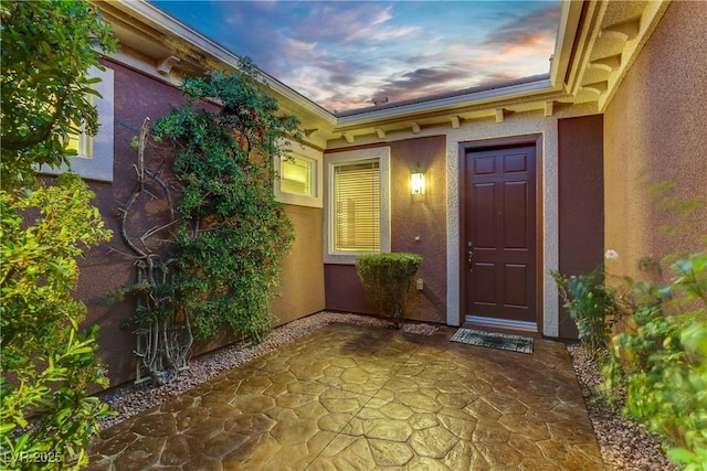 exterior entry at dusk featuring stucco siding and a patio