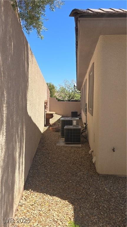 view of side of property featuring stucco siding, a fenced backyard, and central AC