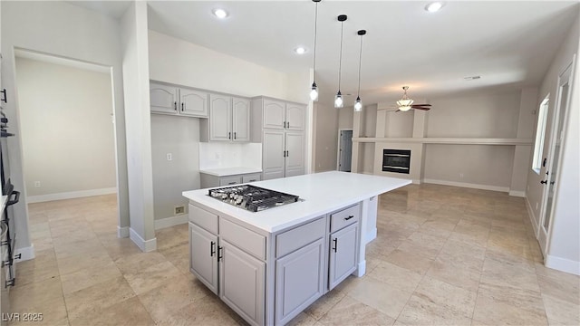 kitchen featuring stainless steel gas stovetop, ceiling fan, a center island, hanging light fixtures, and light countertops